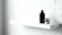 Minimalist white shelf mounted on brick wall displaying black bottle, small potted plant, and candle in monochrome interior design setting.