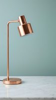 Copper desk lamp with adjustable cylindrical shade on marble surface against muted teal background, suitable for interior design and home decor projects.