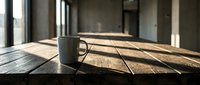 Mug with hot beverage sitting on wooden table in modern loft space with sunlight streaming through windows, creating dramatic shadows for lifestyle and workspace concepts.