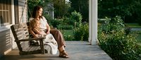 Young woman relaxing on wooden porch swing in peaceful garden setting during golden hour sunlight for lifestyle and wellness concepts.
