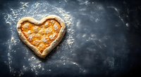 Heart-shaped homemade pizza with cheese topping on dark rustic background with flour dusting, symbolizing love for Italian cuisine.