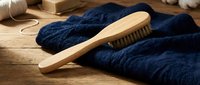 Wooden clothes brush with natural bristles on navy blue knitted sweater, garment care and maintenance concept for sustainable fashion and textile cleaning.