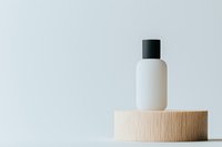 White cosmetic bottle with black cap on wooden podium against light background, minimalist product photography for beauty and skincare marketing.