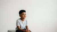 Young Black male child, approximately 8-12 years old, wearing casual gray t-shirt, smiling and looking to the side against neutral white background, suitable for educational, family, and lifestyle content.
