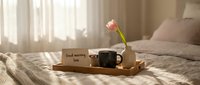Cozy morning bedroom scene with coffee mug, pink tulip flower and good morning note on wooden tray in soft sunlight for lifestyle and home decor concepts.