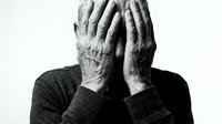 Elderly man covering face with wrinkled hands expressing stress, depression, grief or shame in black and white emotional portrait for mental health awareness.