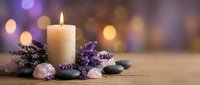 Burning candle with lavender flowers and spa stones on wooden surface with soft bokeh lights background creating peaceful wellness atmosphere.