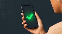 Person with medium skin tone holding smartphone displaying bright green checkmark on dark screen, symbolizing approval, success, confirmation, and completed task verification.