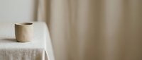 Wooden cup on linen tablecloth with neutral beige curtain backdrop, minimalist home decor and interior design styling.
