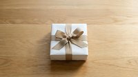White gift box with elegant golden ribbon bow on wooden surface, top view. Minimalist holiday present for birthday, wedding, or celebration.