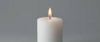 White pillar candle burning with bright flame on neutral gray background for relaxation, meditation, spa treatments, aromatherapy and home decor concepts.