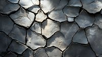 Cracked dry mud texture with deep fissures and natural patterns in dark gray tones, dramatic shadows highlighting surface relief and geometric shapes.