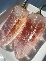 Frozen chili peppers covered in ice crystals on white plate with dramatic lighting and shadows creating refreshing summer food concept.