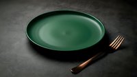 Empty green ceramic plate with bronze fork on dark textured surface, suitable for restaurant menus, food styling, dining concepts, and culinary design projects.
