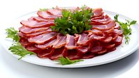 Sliced cured meat platter garnished with fresh parsley on white plate. Traditional cold cuts arranged in circular pattern for appetizer or charcuterie board.