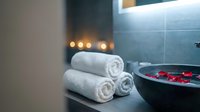 Luxury spa bathroom interior with rolled white towels and floating red rose petals in dark bowl, creating serene wellness atmosphere for relaxation.
