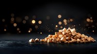 Crushed caramel toffee pieces scattered on dark surface with golden bokeh lights in background, creating luxurious confectionery atmosphere.
