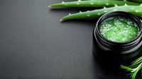 Natural aloe vera gel in black jar with fresh green leaves on dark background for skincare and cosmetic products.