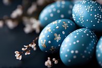 Decorative blue Easter eggs with delicate white and gold floral patterns arranged with spring cherry blossoms on dark background, creating festive holiday mood.