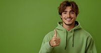 Young man in light green hoodie showing thumbs up gesture with confident smile against vibrant green background, expressing positivity and approval.