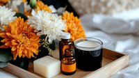 Wellness spa composition with orange and white chrysanthemums, essential oils, natural soap and cream on wooden tray against soft fabric background.
