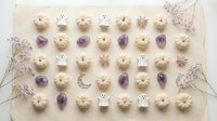 Flat lay arrangement of Halloween cookies with ghosts, pumpkins and purple gems on beige background with dried flowers for autumn baking projects.