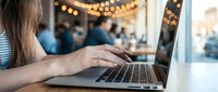 Young woman typing on laptop computer in cozy cafe with warm bokeh lights creating productive workspace atmosphere for remote work and digital lifestyle.