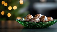 Chocolate truffles with powdered sugar coating arranged in vintage emerald glass bowl against blurred holiday lights and dark background.