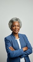 Senior African American woman with gray hair wearing blue blazer and white top, arms crossed, confident professional portrait against neutral background for corporate, business, and leadership applications.