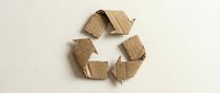 Recycling symbol made from crumpled kraft paper pieces arranged in circular arrow pattern on neutral background, representing sustainability and eco-friendly practices.