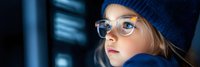 Young blonde woman programmer in glasses and blue beanie working late at computer screen in dark office environment for technology and coding projects.