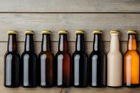 Row of assorted beer bottles with gold caps arranged on rustic wooden background, showing variety of dark and light craft brews for beverage industry marketing.