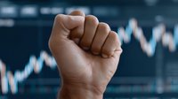 Raised fist against blurred financial chart background symbolizing market strength, investment power, trading success, economic determination and business victory.