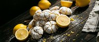 Freshly baked lemon crinkle cookies dusted with powdered sugar arranged on rustic wooden board with bright yellow lemons and linen napkin for baking content.