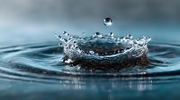 Water drop creating splash crown with ripples on calm blue surface capturing moment of impact in macro photography.