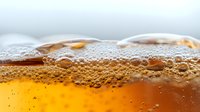 Macro shot of golden bubbles and foam in carbonated beverage against blurred background, showing refreshing effervescent texture and amber liquid surface.