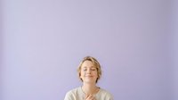 Young man with blonde wavy hair and fair complexion wearing beige sweater against purple background, looking upward with positive expression for lifestyle and portrait use.