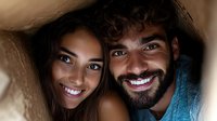 Young mixed-race couple with bright smiles close up portrait in warm low key lighting. Bearded man and Asian woman share intimate moment.