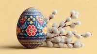 Traditional Ukrainian pysanka Easter egg with intricate folk patterns and pussy willow branches on warm beige background for spring holiday celebrations.