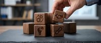 Hand placing wooden cube with gear icon among business strategy blocks on slate surface for corporate planning and development concepts.