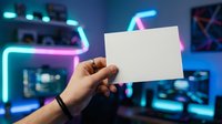 Caucasian male hand holding blank white card in neon-lit gaming room with glowing cyan and pink lights, computer setup, and digital displays in background.