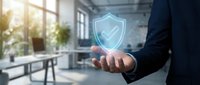 Professional businessman holding glowing digital security shield with checkmark in modern office environment representing cybersecurity and data protection.