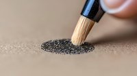 Forensic brush dusting black fingerprint powder on textured surface, revealing detailed ridge patterns in criminal investigation macro photography.