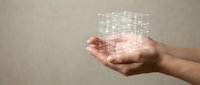 Hands holding holographic digital cube with glowing grid pattern representing data visualization, technology innovation and futuristic computing concepts.