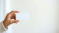Hand holding blank white business card against neutral background for branding and corporate identity mockup purposes.