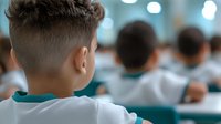 Students sitting in classroom during exam or test, view from behind focusing on boy in turquoise shirt. Blurred background shows other students concentrating.