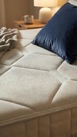 Cozy bedroom scene featuring a quilted beige mattress with navy blue pillow, warm bedside lamp, ceramic mug, and soft textiles for home decor and lifestyle content.