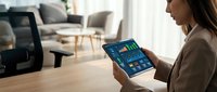Young Asian businesswoman analyzing financial dashboard with colorful charts and graphs on tablet in modern office interior.