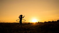 Woman silhouette spinning hula hoop in golden sunset field, outdoor fitness and recreational activity during golden hour.