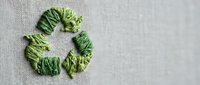 Green recycling symbol made from natural leaves on neutral linen fabric background representing eco-friendly sustainability and environmental conservation concept.